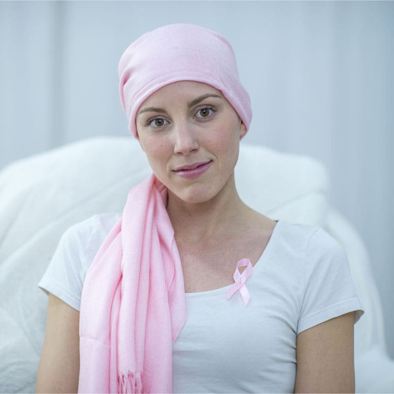 Portrait of a woman wearing a pink headscarf and a pink breast cancer awareness ribbon on her shirt.