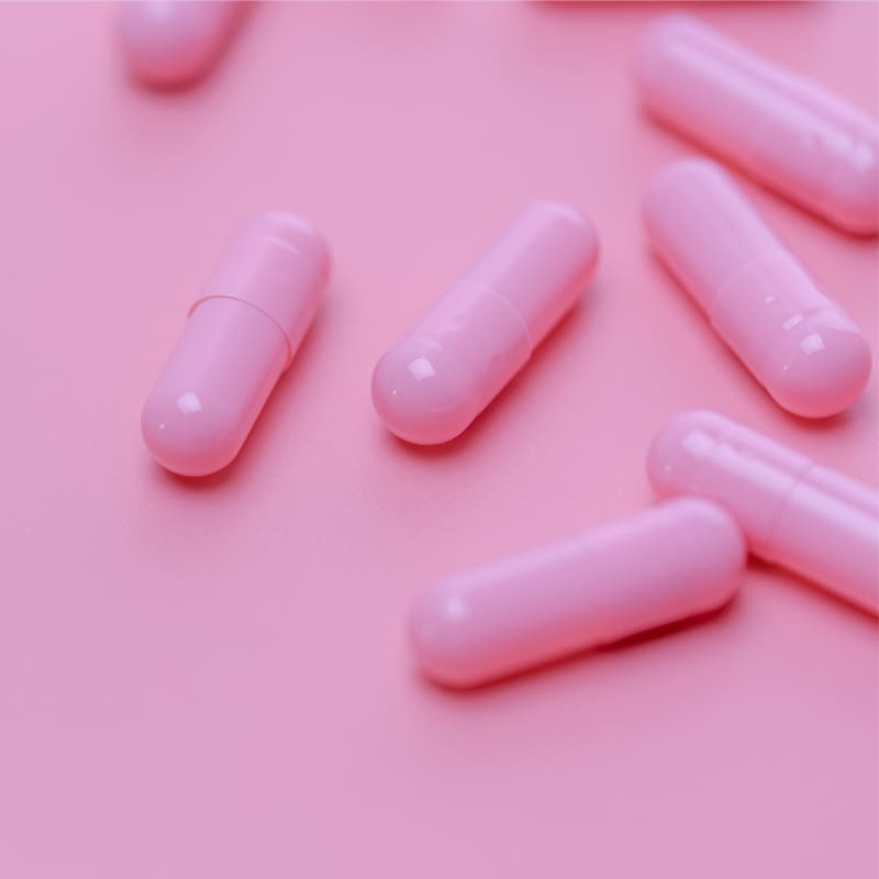 Close-up of several medication capsules on a pink background.